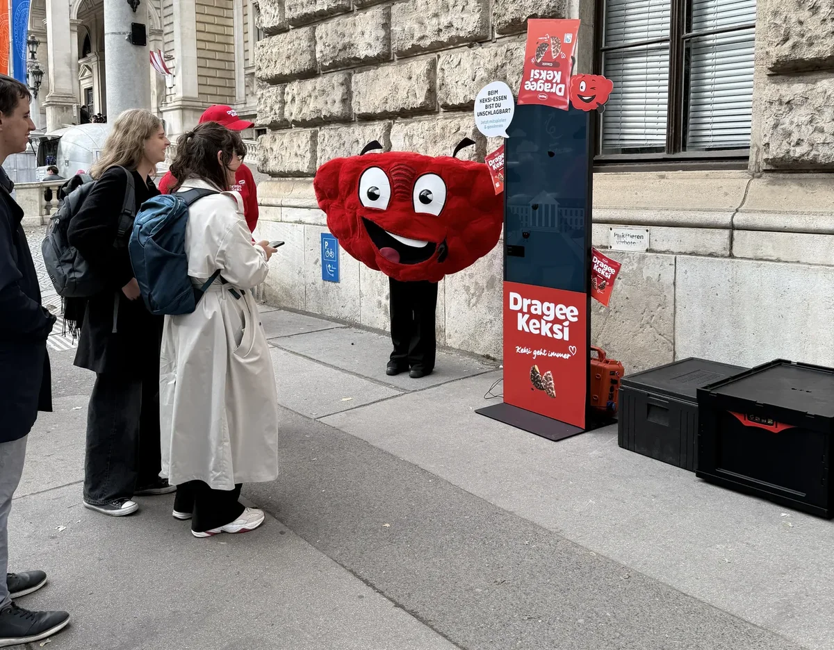 Students in front of a university in Vienna at the Dragee Keksi game kiosk, next to the red cookie mascot and the campaign line "Keksi geht immer".